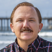 Headshot of a smiling man with brown hair and a mustache, with the Huntington Beach Pier in the background.