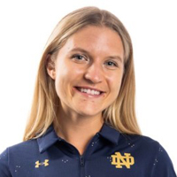 Headshot of a smiling young woman with blonde hair, wearing a blue Polo shirt bearing the insignia of Notre Dame University.