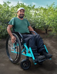 A thumbnail image of a Guatemalan man in a new, blue wheelchair, on an unpaved path through green foliage.