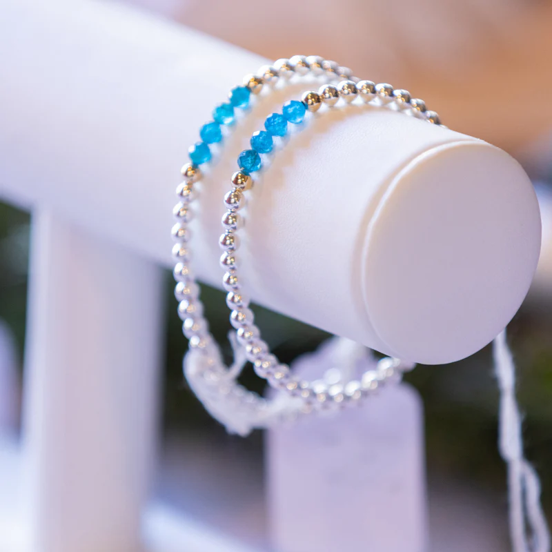 Two Dignity bracelets, made of silver beads with four blue beads on it, on a display.
