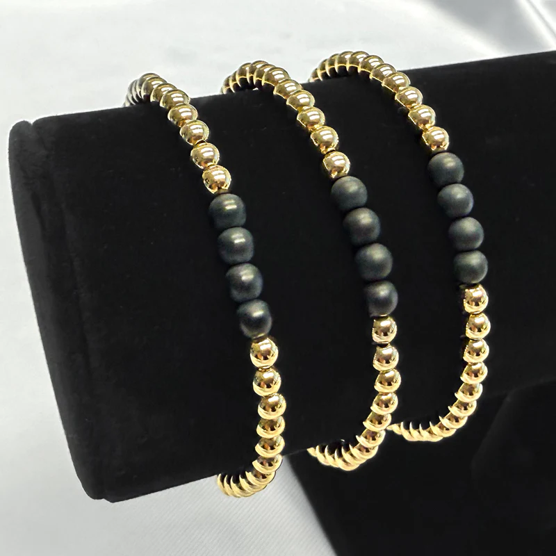 Three Joy bracelets for women, made of gold and black beads, on a display.s