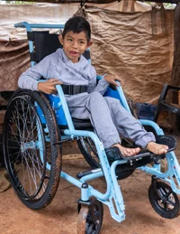 A Brazilian boy in a new blue wheelchair, smiling.